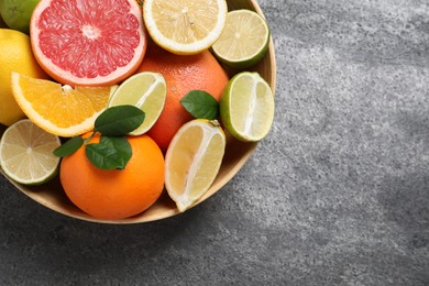 Photo of Different fresh citrus fruits and leaves in bowl on grey textured table, top view. Space for text