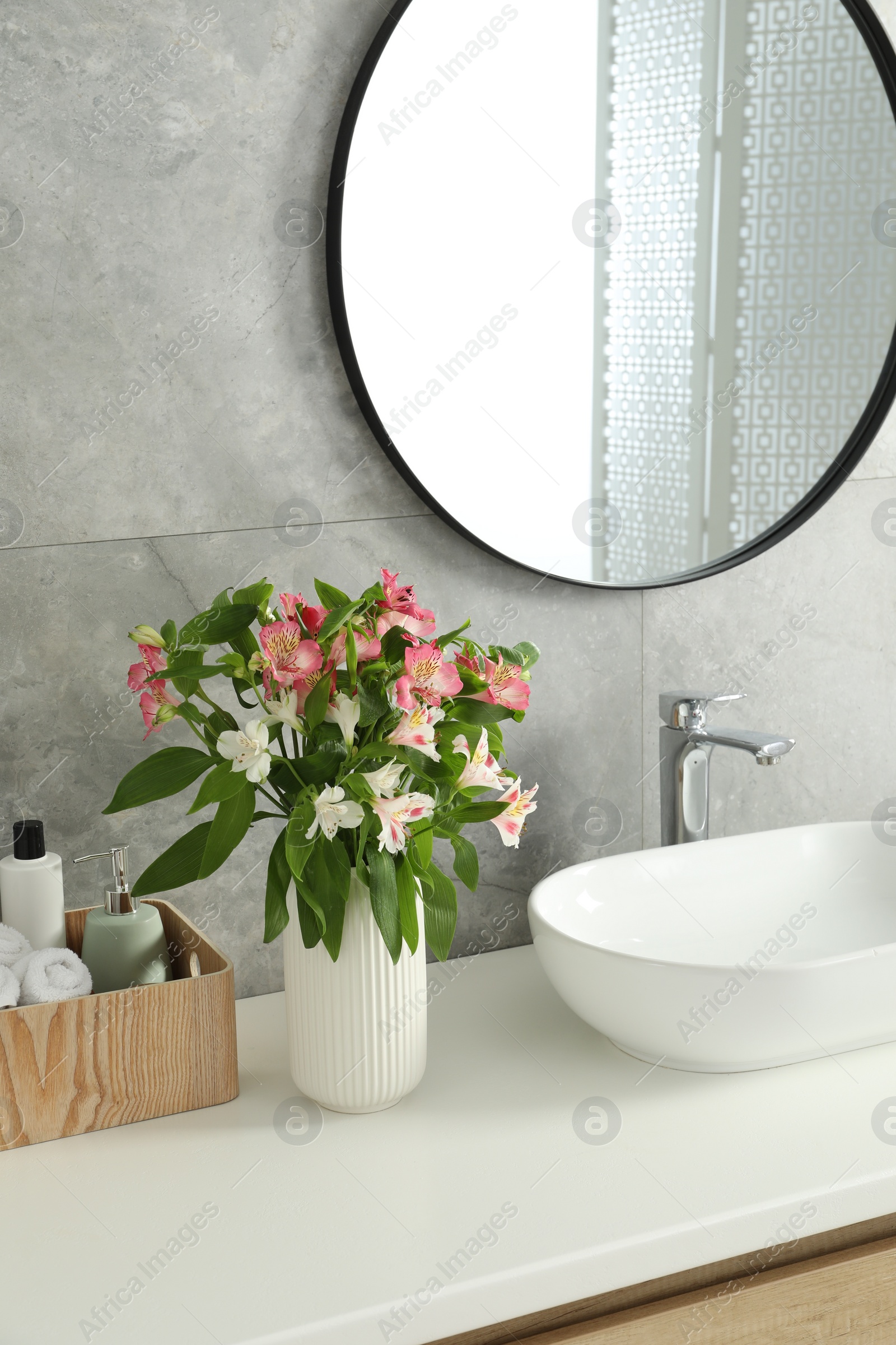 Photo of Vase with beautiful Alstroemeria flowers and toiletries near sink in bathroom