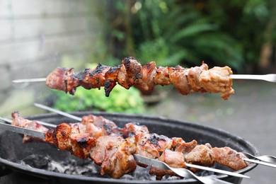 Photo of Cooking delicious kebab on metal skewers outdoors