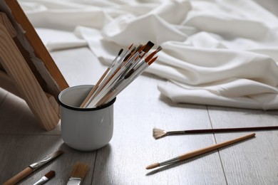Photo of Different brushes near stand with canvas on floor in artist's studio, space for text