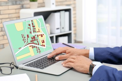 Man analyzing cadastral map on laptop at table, closeup 
