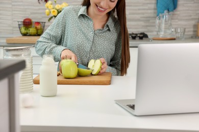 Photo of Young woman making apple cake while watching online cooking course via laptop in kitchen, closeup. Time for hobby
