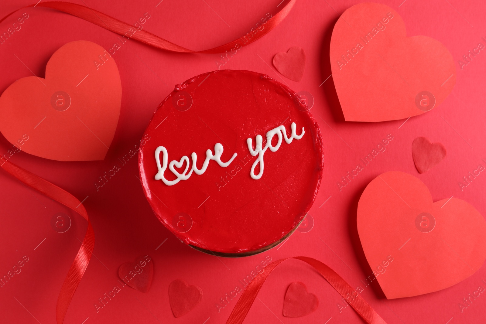 Photo of Bento cake with text Love You, ribbon and paper hearts on red table, flat lay. St. Valentine's day surprise