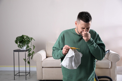 Photo of Man with vacuum cleaner bag suffering from dust allergy at home