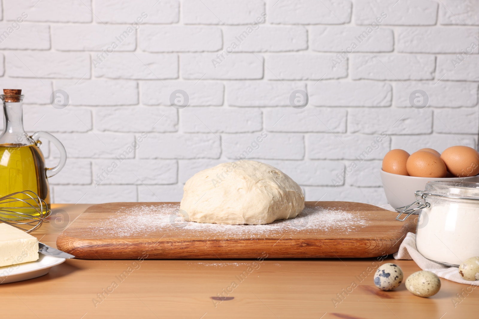 Photo of Fresh dough sprinkled with flour and other ingredients on wooden table near white brick wall