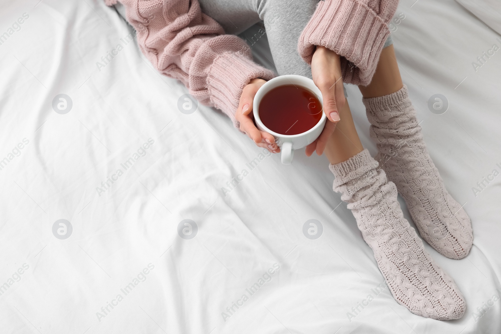 Photo of Woman with cup of tea wearing warm socks in comfortable bed, closeup. Space for text