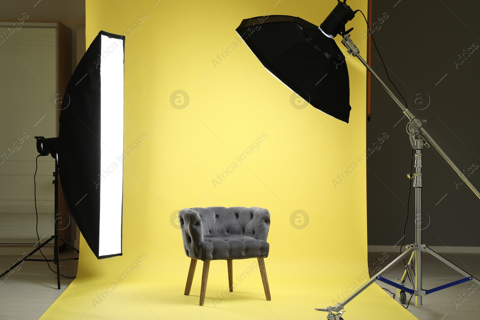 Photo of Yellow photo background, armchair and professional lighting equipment in modern studio