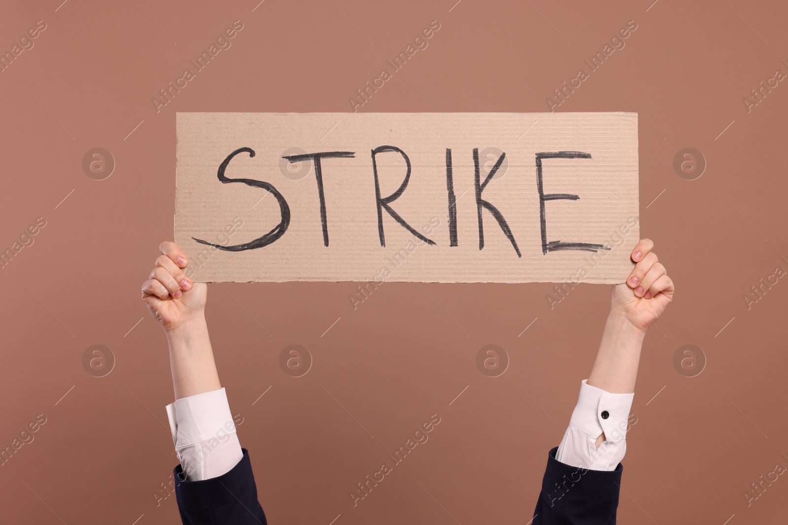 Photo of Woman holding cardboard banner with word Strike on brown background, closeup