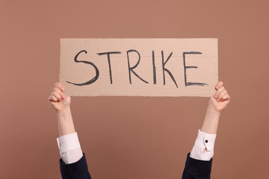 Woman holding cardboard banner with word Strike on brown background, closeup