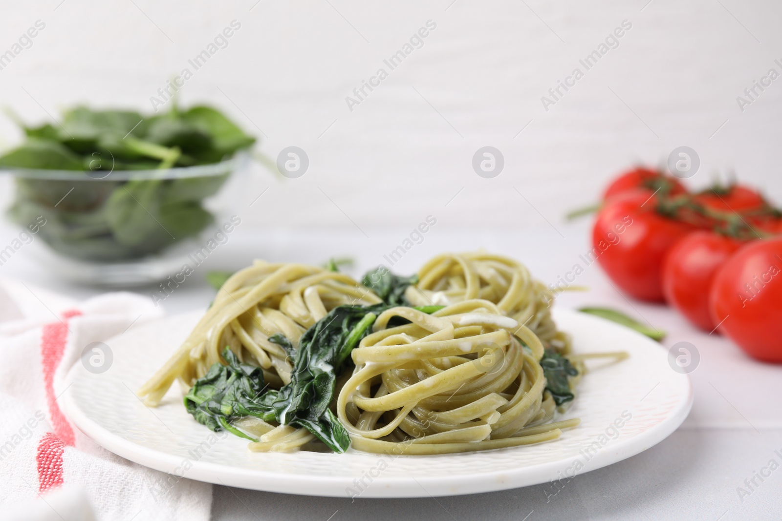 Photo of Tasty pasta with spinach and sauce on white tiled table, closeup