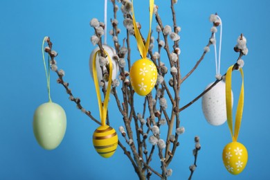 Photo of Beautiful willow branches with painted eggs on light blue background, closeup. Easter decor