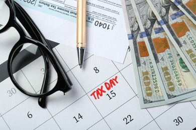 Photo of Calendar with date reminder about tax day, documents, money, pen and glasses, top view