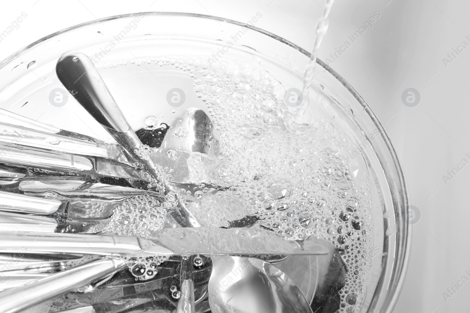 Photo of Washing silver spoons, forks and knives under stream of water in kitchen sink, above view