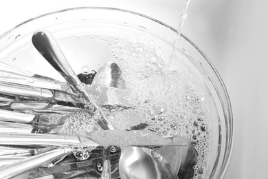 Photo of Washing silver spoons, forks and knives under stream of water in kitchen sink, above view