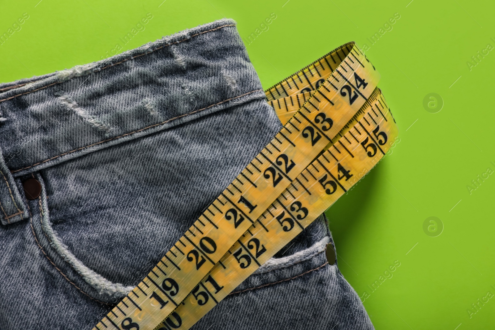 Photo of Jeans with measuring tape on green background, top view. Weight loss concept