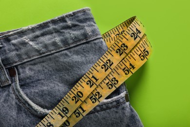 Jeans with measuring tape on green background, top view. Weight loss concept