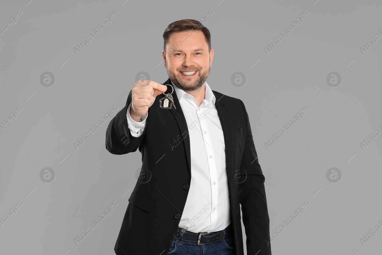 Photo of Male real estate agent holding key on grey background