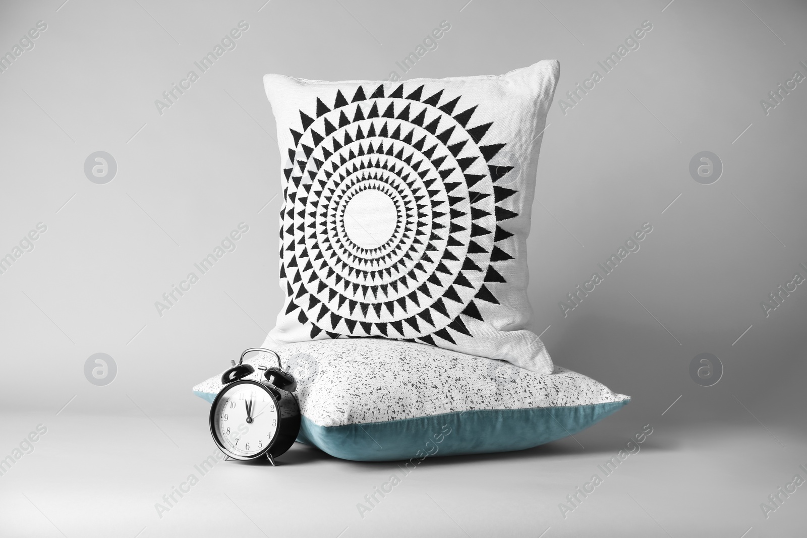 Photo of Soft decorative pillows and alarm clock on light background