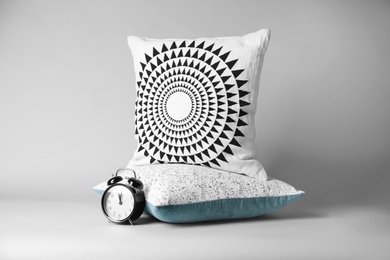 Photo of Soft decorative pillows and alarm clock on light background