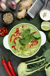 Saucepan with delicious green curry chicken soup and different ingredients on grey table, flat lay