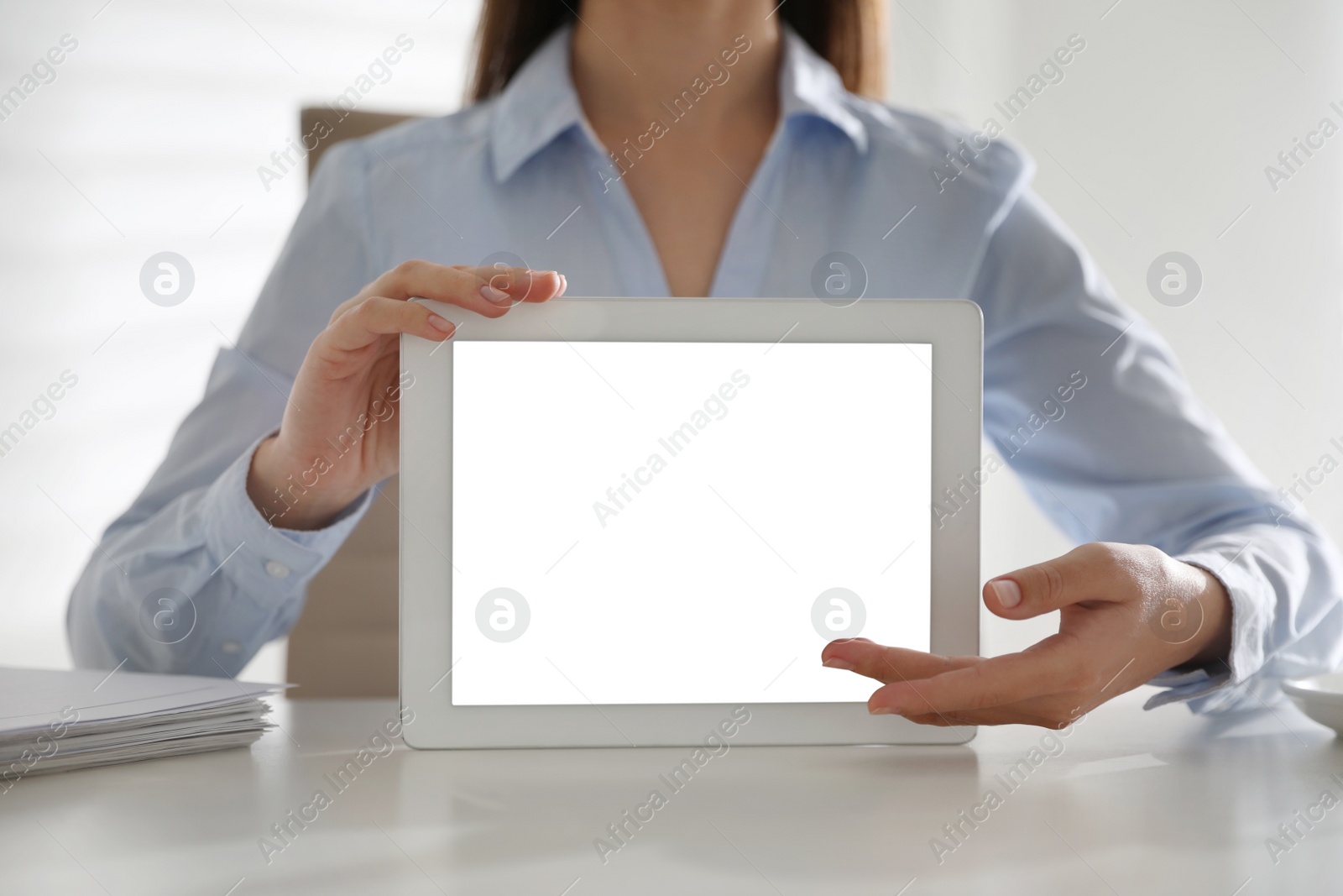 Photo of Businesswoman holding modern tablet with blank screen at white table in office, closeup
