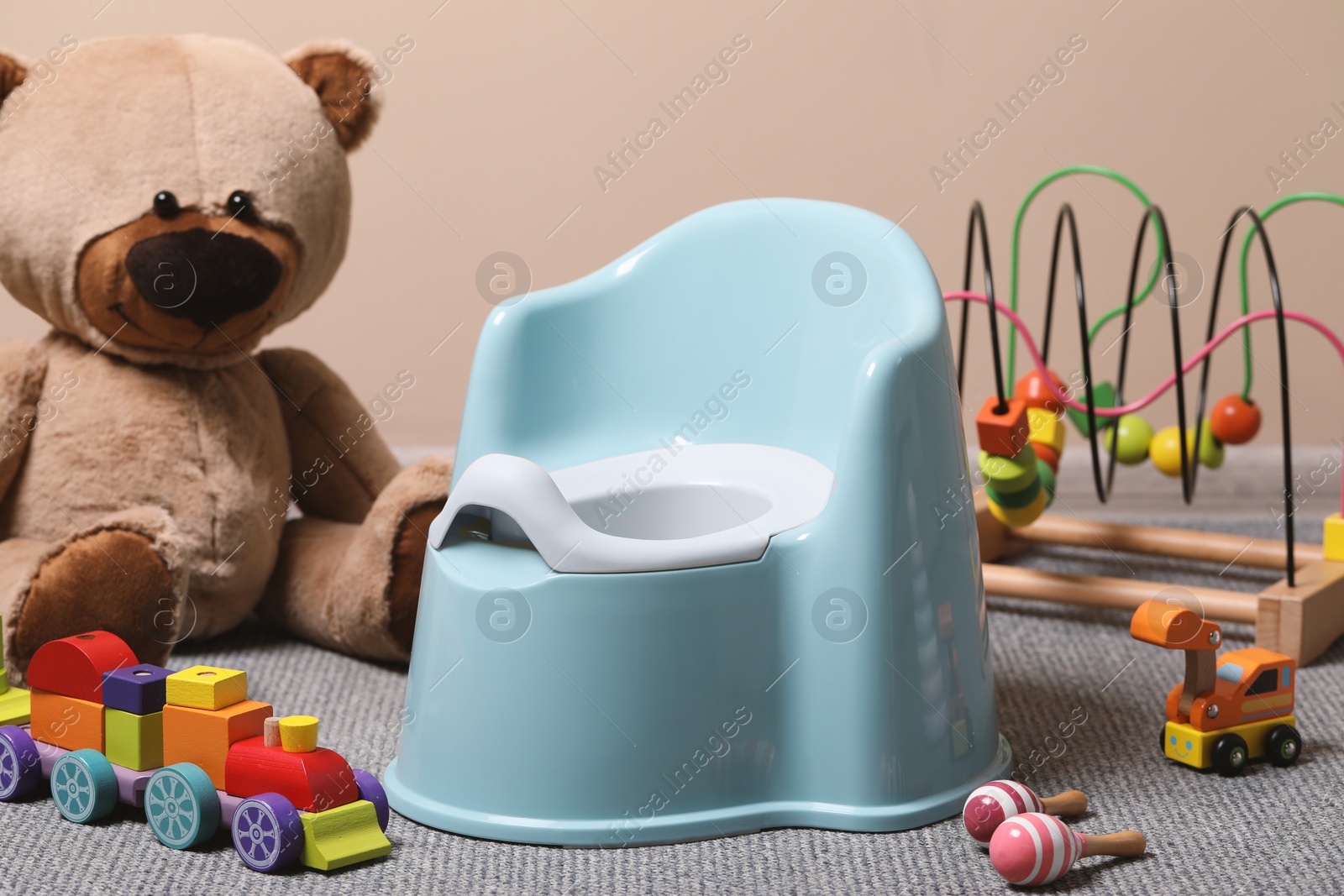 Photo of Light blue baby potty and toys on carpet near brown wall. Toilet training