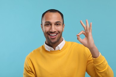 Smiling man with healthy clean teeth showing ok gesture on light blue background