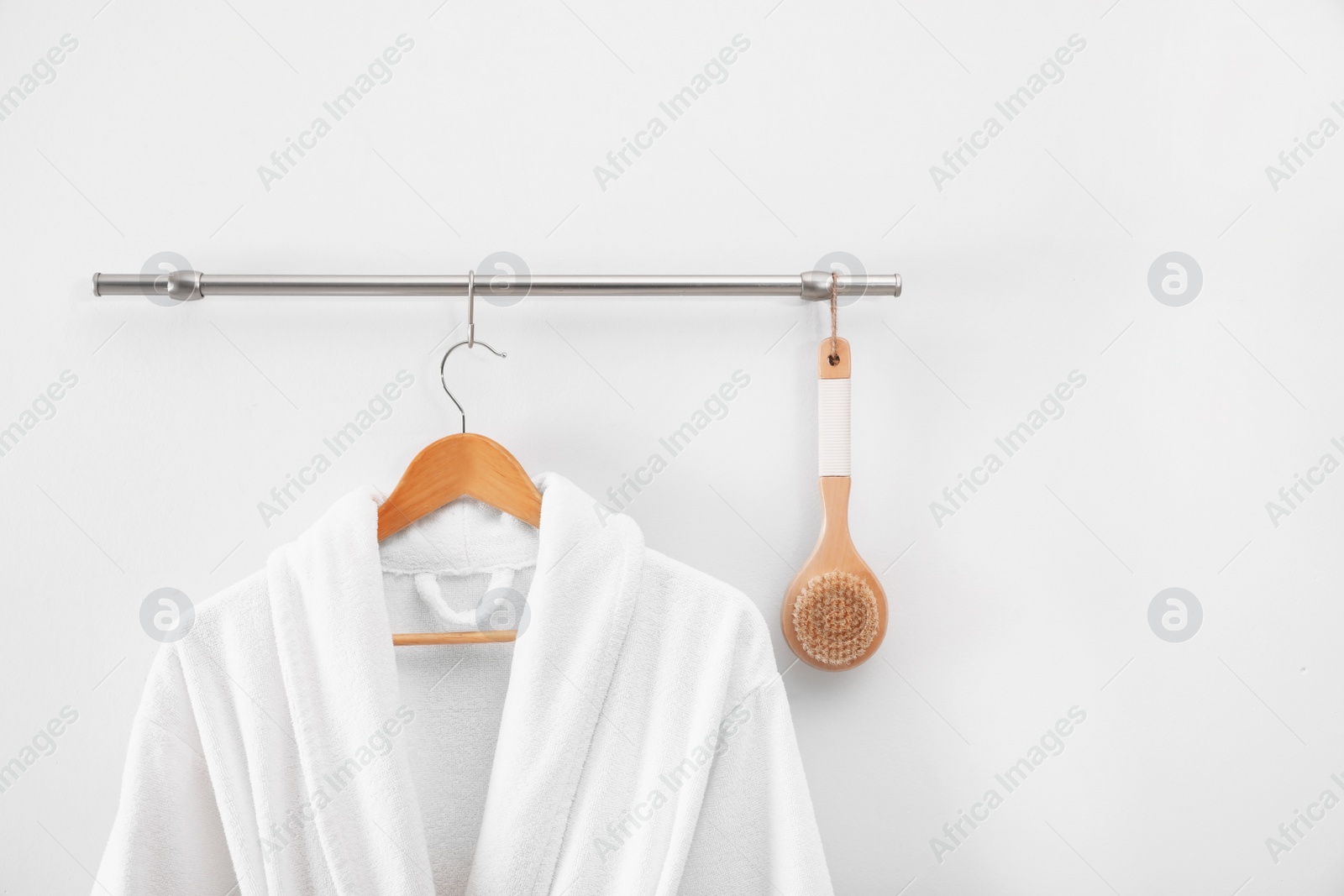 Photo of Hanger with clean bathrobe and brush on light wall