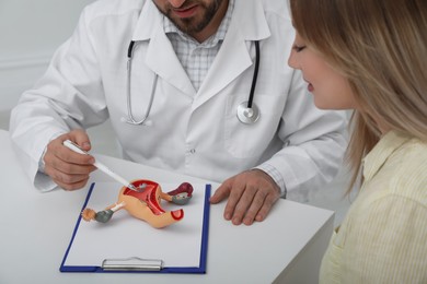 Photo of Gynecologist demonstrating model of female reproductive system to young woman in clinic, closeup