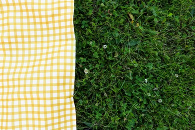 Photo of Checkered picnic tablecloth on fresh green grass, top view. Space for text