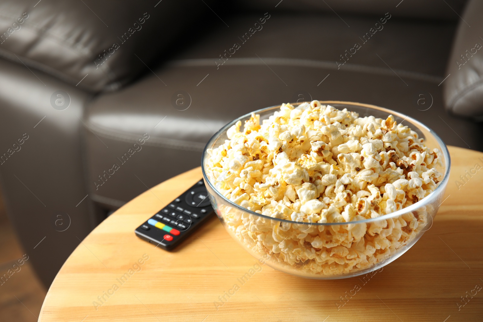 Photo of Bowl of popcorn and TV remote on table against blurred background. Watching cinema