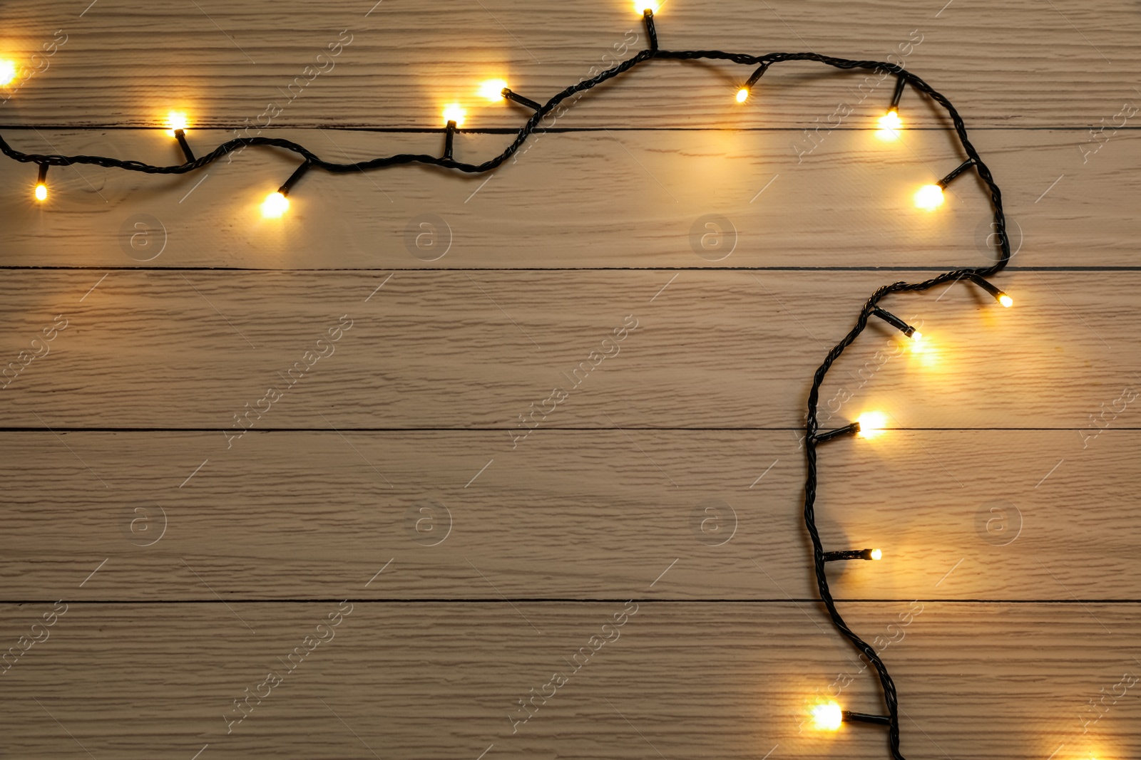 Photo of Glowing festive lights on wooden background, top view. Space for text