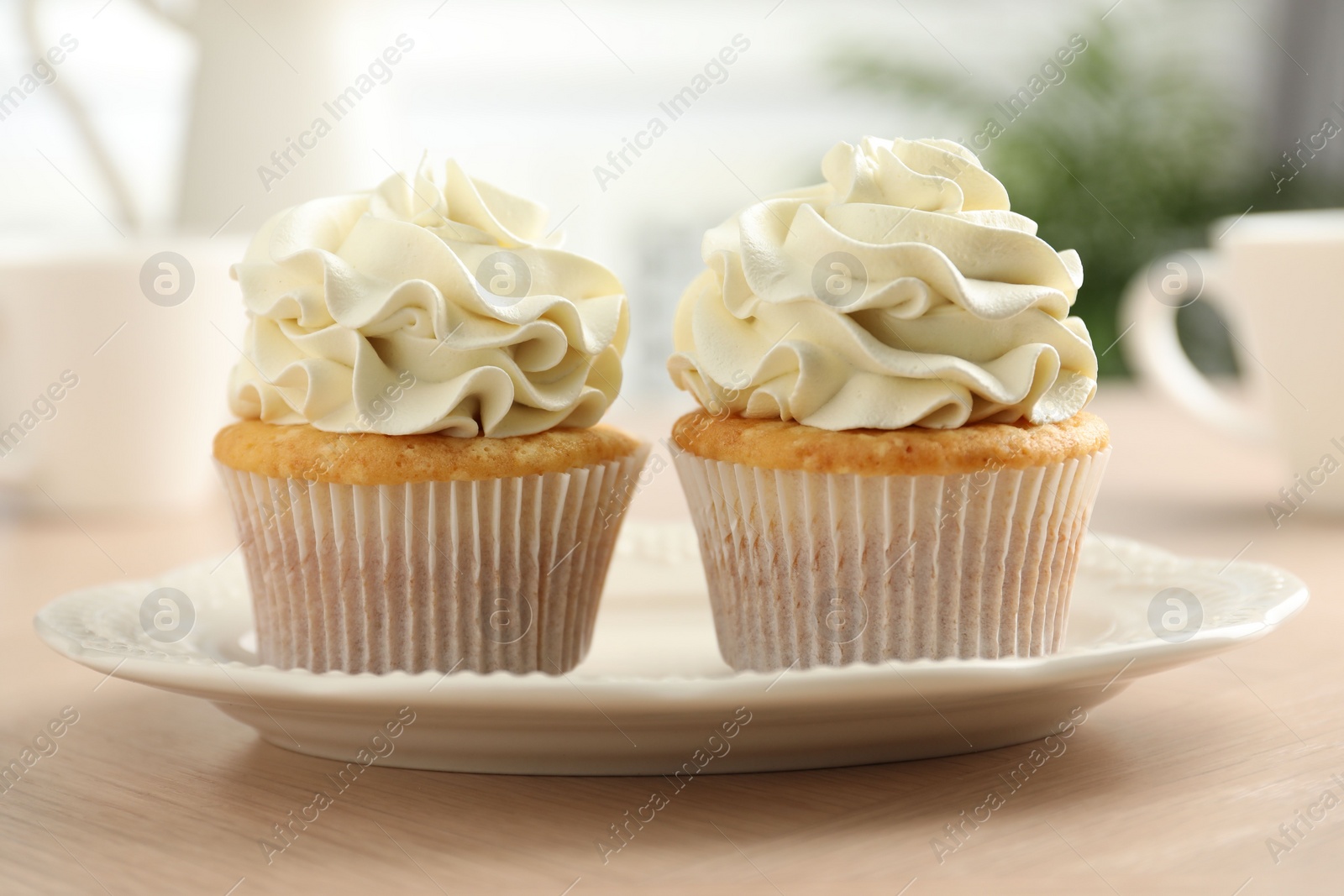 Photo of Tasty cupcakes with vanilla cream on light wooden table, closeup