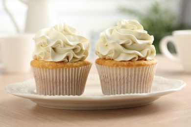 Tasty cupcakes with vanilla cream on light wooden table, closeup