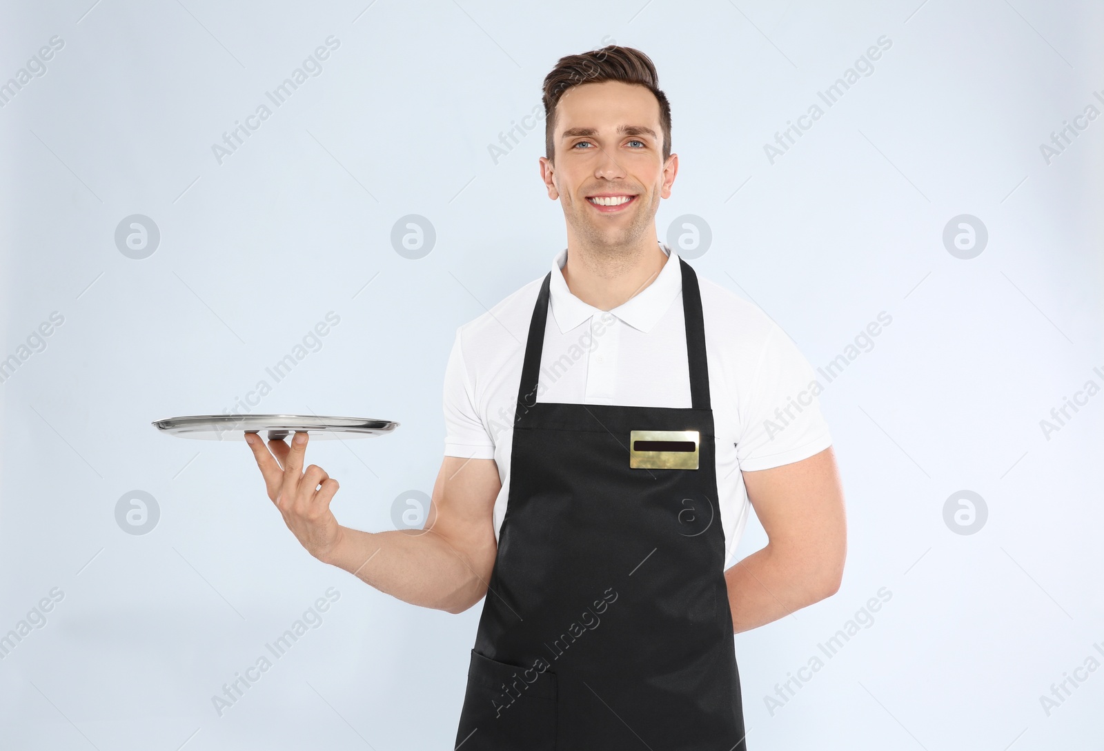 Photo of Handsome waiter with empty tray on light background