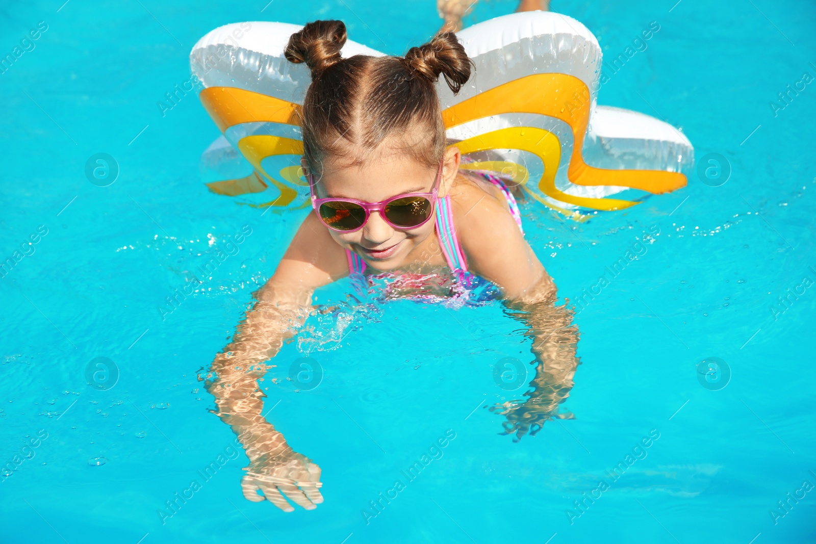 Photo of Little girl with inflatable ring in swimming pool on sunny day