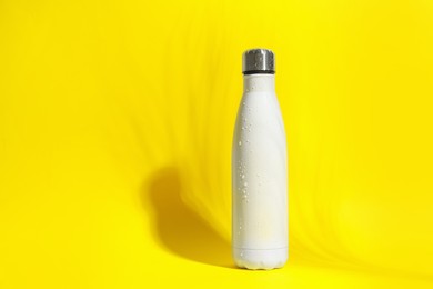 Photo of Stylish white thermo bottle with water drops on yellow background, space for text