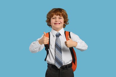 Photo of Happy schoolboy with backpack showing thumbs up gesture on light blue background