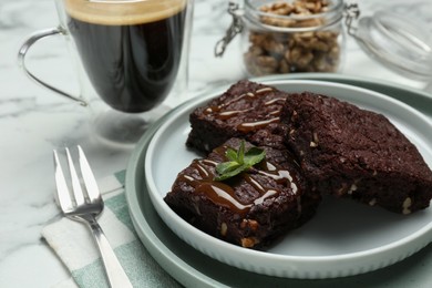 Delicious chocolate brownies with nuts, caramel sauce and fresh mint on white marble table, closeup