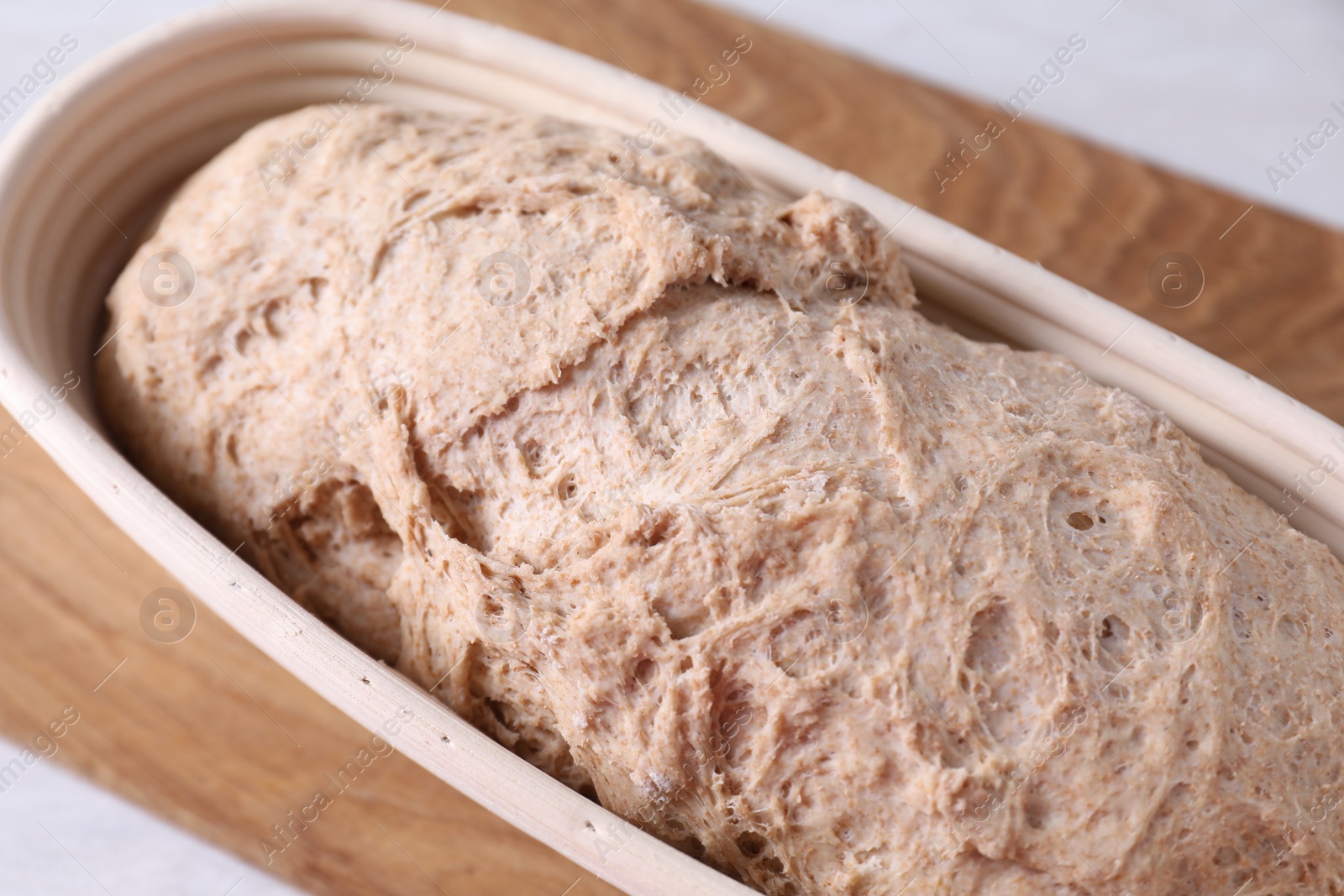 Photo of Fresh sourdough in proofing basket on table, closeup