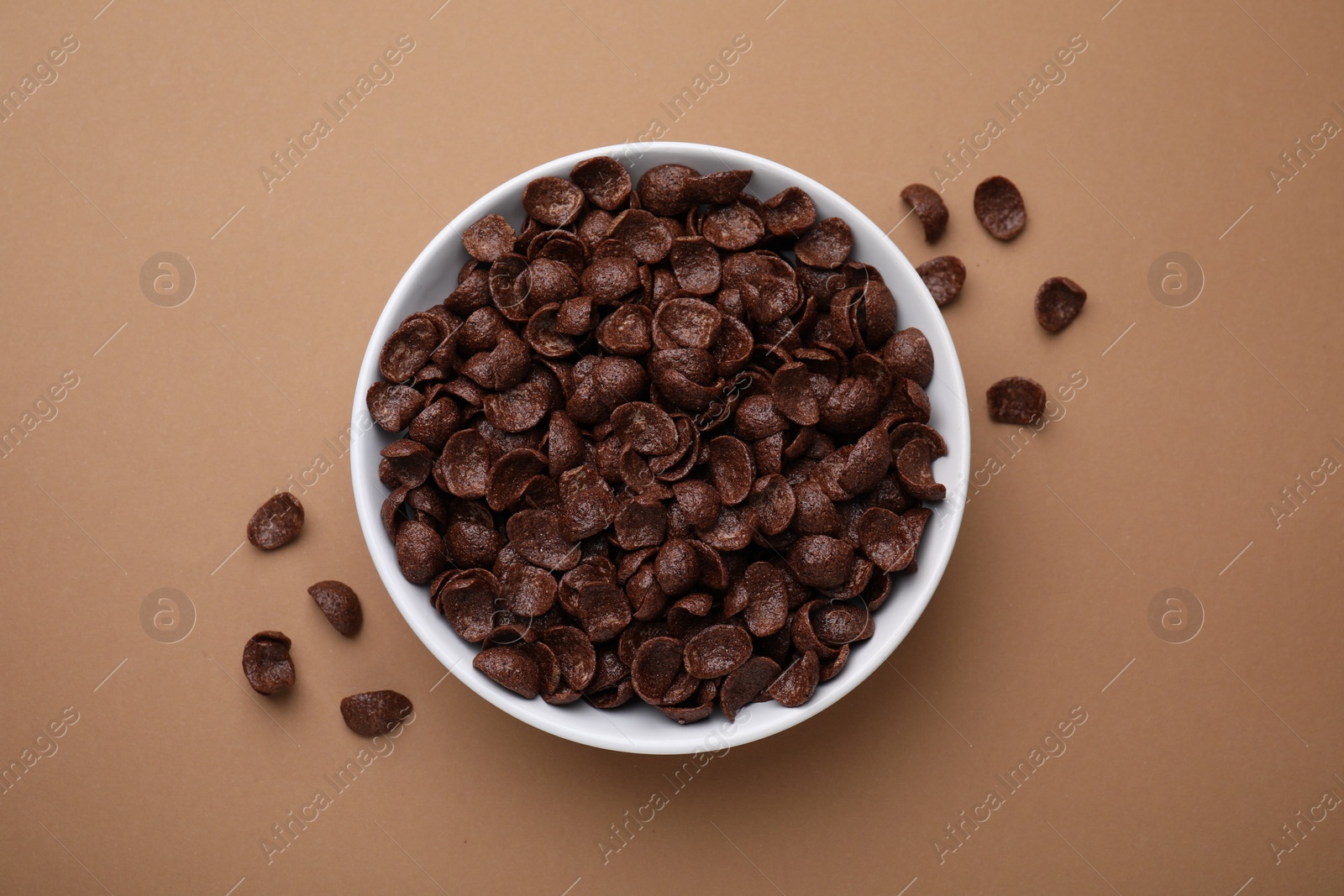 Photo of Breakfast cereal. Chocolate corn flakes in bowl on brown table, top view