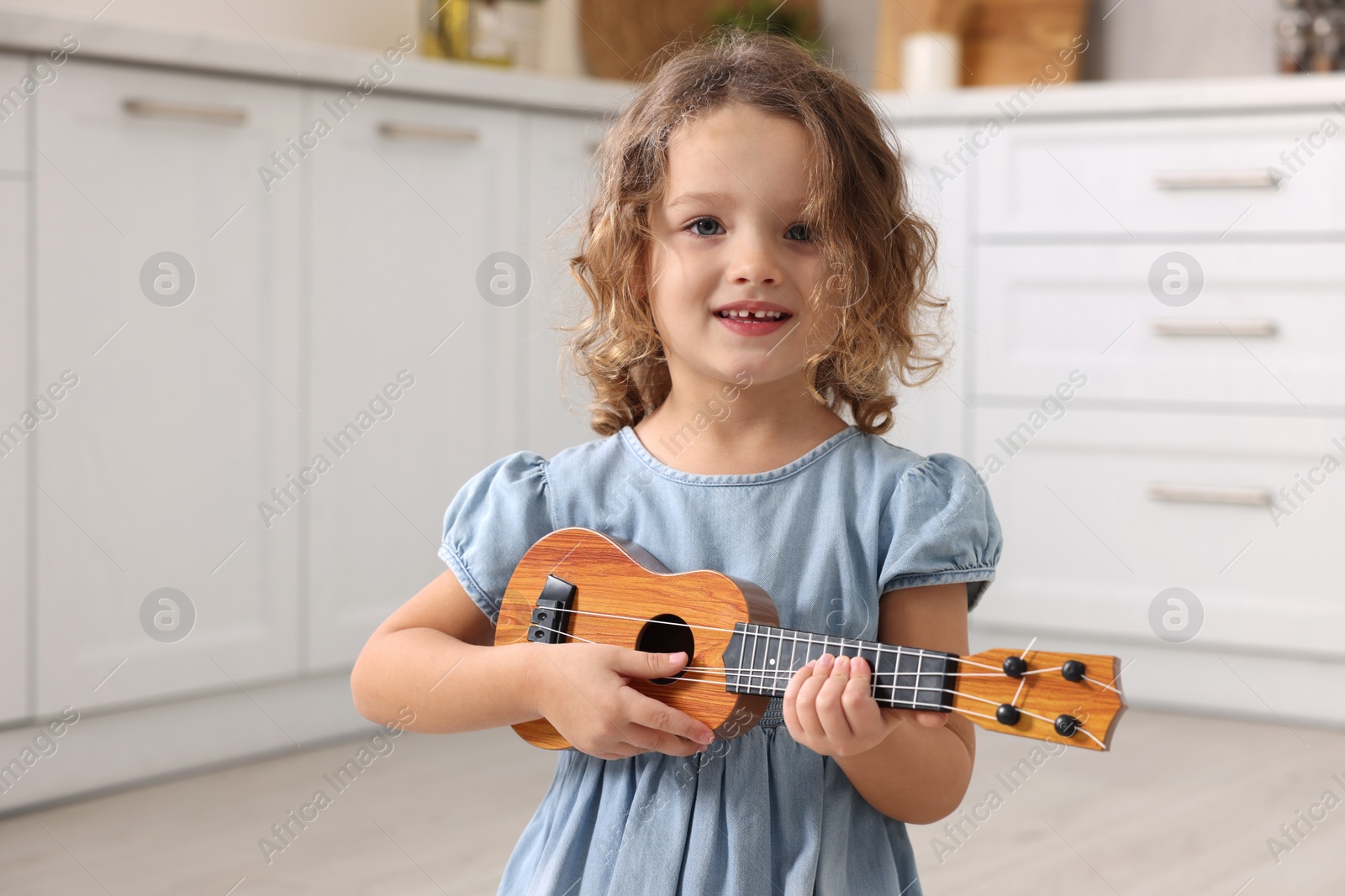 Photo of Little girl playing toy guitar in kitchen