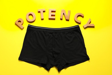 Photo of Men underwear and word Potency made of wooden letters on yellow background, flat lay