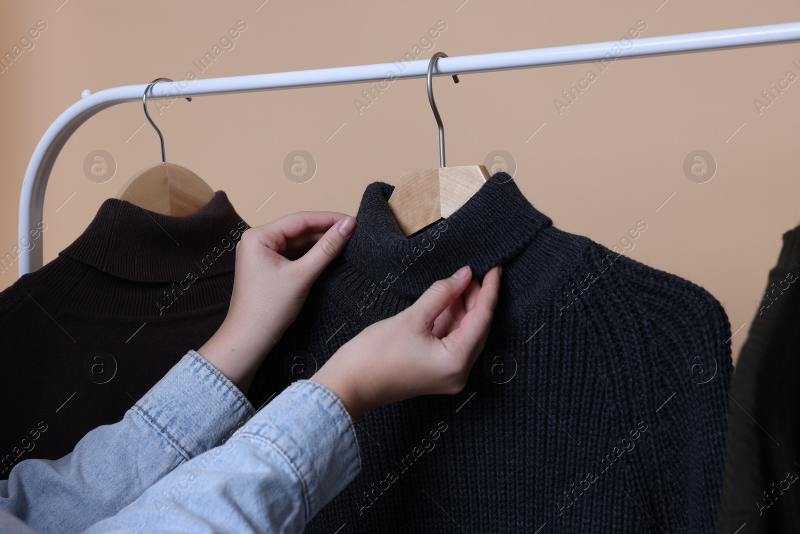 Photo of Woman taking sweater from rack on beige background, closeup