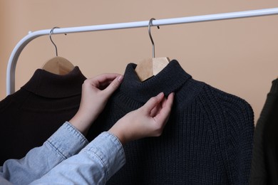Woman taking sweater from rack on beige background, closeup