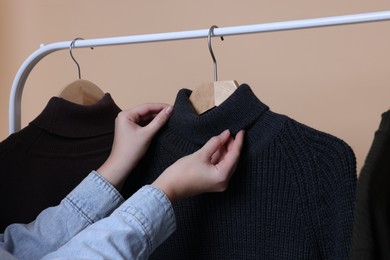 Photo of Woman taking sweater from rack on beige background, closeup