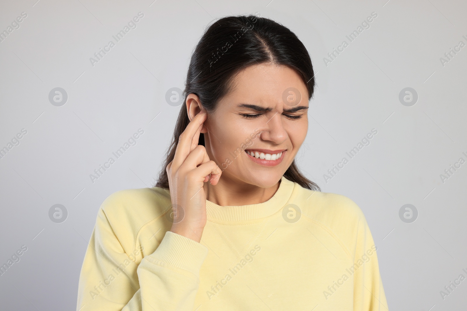 Photo of Young woman suffering from ear pain on light grey background