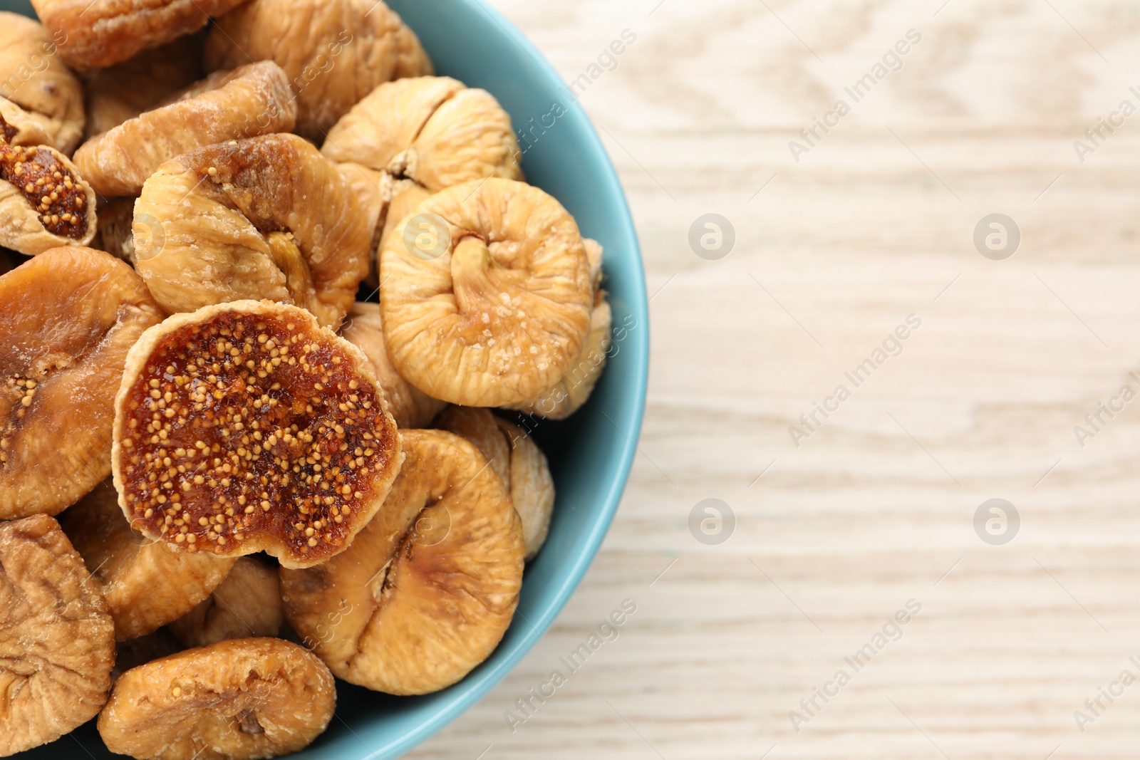 Photo of Bowl with tasty dried figs on white wooden table, top view. Space for text