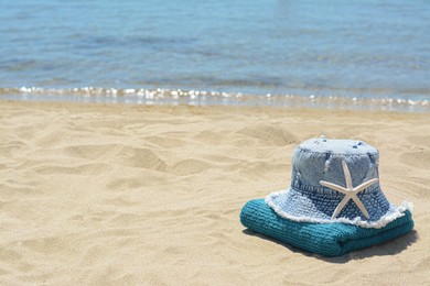 Photo of Stylish denim hat, towel and starfish on sand near sea, space for text. Beach accessories