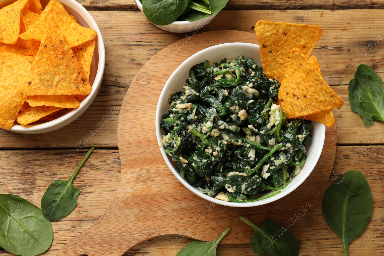 Photo of Tasty spinach dip with eggs in bowl and nachos chips on wooden table, flat lay